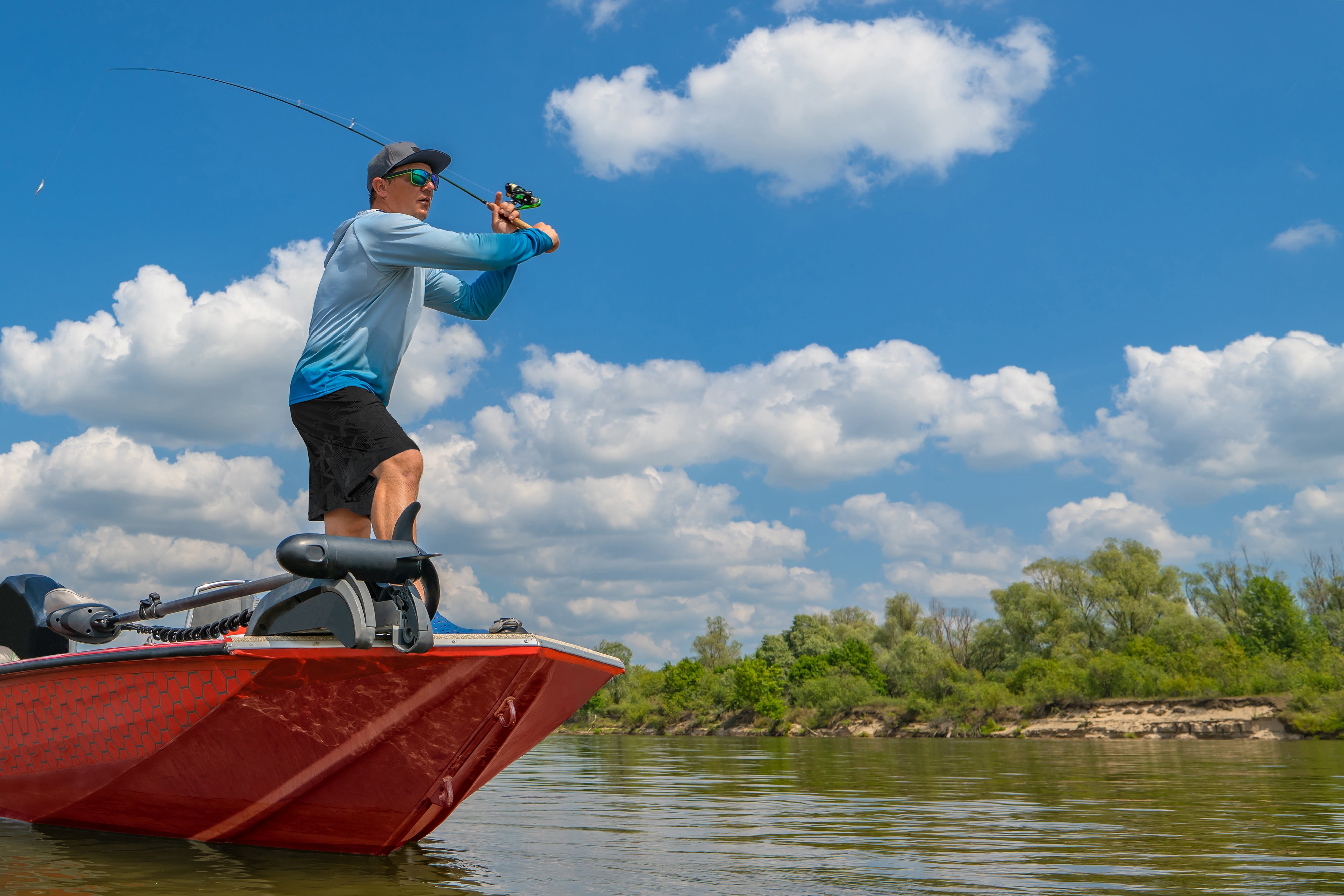 Fisherman on boat make a cast by fishing rod at wild river